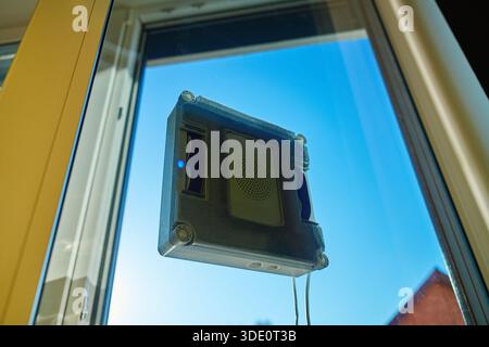 Square window cleaning robot washing glass. Robotic window cleaner working on window surface against blue sky. Smart home appliance concept Stock Photo