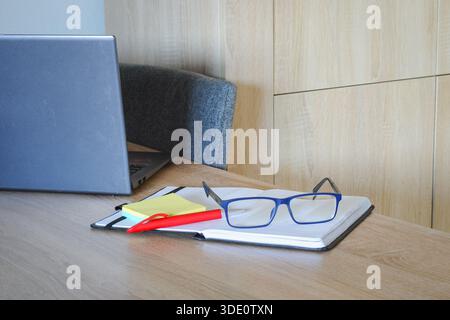 Eyeglasses and notebook on wooden desk with laptop in modern workspace Stock Photo