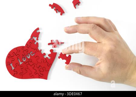 a hand putting together a heart-shaped puzzle Stock Photo