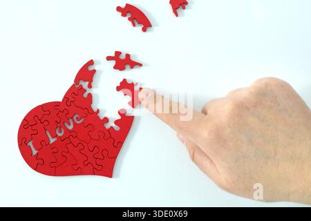 a hand putting together a heart-shaped puzzle Stock Photo