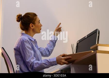 Side view of female in shirt pointing index finger up and clutching box on office counter. Stock Photo
