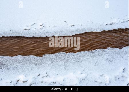 Minimalist abstract composition showing flowing brown water stream bordered by white snow and ice formations. Stock Photo