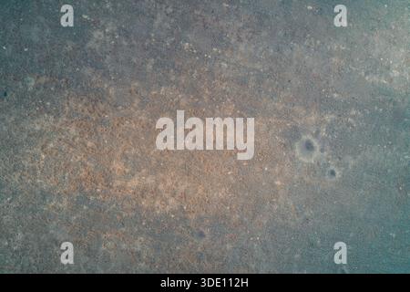 Minimalist aerial top view of a textured frozen surface covered in brown sediment. The gritty grunge pattern with blue-grey tones and small craters creates a unique abstract background resembling concrete, stone, or old paper. Copy space. Stock Photo
