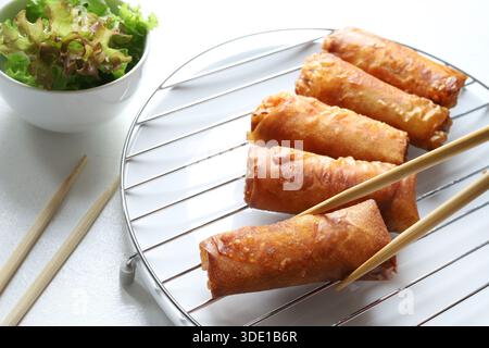 Crispy fried spring rolls (Chinese rolls) served with chopsticks and fresh lettuce on a white background. Typical dish of Asian cuisine. Overhead view. Stock Photo