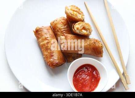 Plate with crispy fried spring rolls (Chinese rolls) served with chopsticks and red sauce on a white background. Typical dish of Asian cuisine. Stock Photo