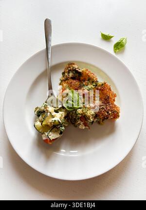 A white plate with a slice of vegetable omelette isolated on a white wooden background. Overhead view. Stock Photo