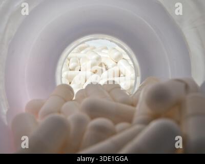 White Capsules Seen From Inside a Medication Bottle; Unique perspective looking down into a container filled with numerous white capsules. Represents Stock Photo