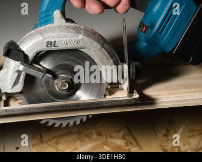 Close-up of Cordless Circular Saw Cutting Wood; Detail close-up of a carpenter using a powerful cordless circular saw to cut precise lines through a s Stock Photo