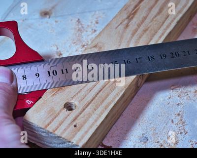 Woodworker Measuring Plank with Marking Gauge; Close-up of a carpenter using a red precision marking gauge and ruler to measure and mark raw wooden pl Stock Photo