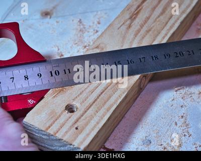 Woodworker Measuring Plank with Marking Gauge; Close-up of a carpenter using a red precision marking gauge and ruler to measure and mark raw wooden pl Stock Photo