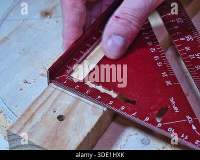 Accurate measurement using a speed square tool; Close-up of a carpenter using a red aluminum speed square to mark or measure wood during a constructio Stock Photo