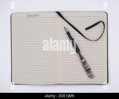 Top down view of an open notebook featuring a January planning heading, a clear fountain pen, and a black ribbon marker on a clean white surface. Stock Photo