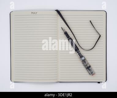 Flat lay shot of an open notebook with a May heading, demonstrator fountain pen, and black ribbon bookmark on a clean white surface. Stock Photo
