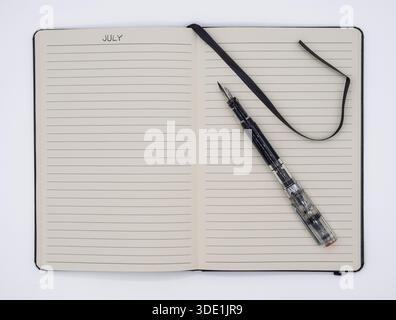 Top view of a blank lined journal opened to the July section with a transparent fountain pen on a neutral background. Stock Photo