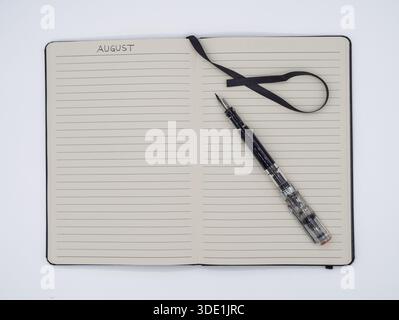 Lined notebook page for August with a modern fountain pen and a black ribbon marker on a clean white surface. Stock Photo