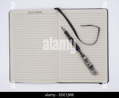 A top-down view of an open lined journal with the month of December written at the top and a fountain pen resting on the page. Stock Photo
