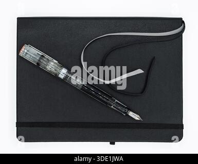 High angle shot of a minimalist black notebook and a modern transparent fountain pen on a white background. Stock Photo