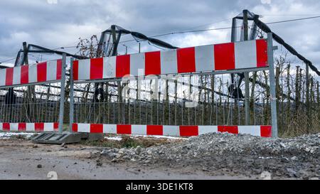 Red and white barrier stands at a winter construction site with stones and scaffolding under a gray sky Stock Photo