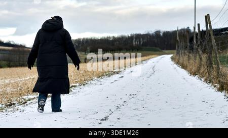A person walks along a snow-covered path in a rural landscape, surrounded by winter scenery Stock Photo