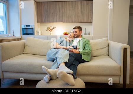 Happy couple man and woman relaxing hugging on couch at home, enjoying peaceful moments together. Stock Photo