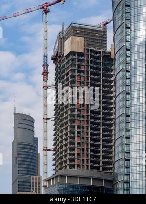 High scrapper under construction. A skeleton of high rise building with the crane mounted to the construction. Finished buildings on the background. N Stock Photo