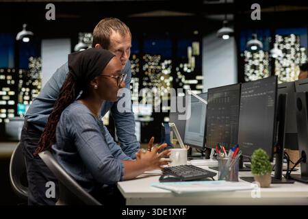 Manager assisting tech startup intern coding advanced artificial intelligence algorithms. Team leader helping worker in office using machine learning models to do automation Stock Photo