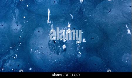Frozen water displays intricate patterns of cracked ice and trapped air bubbles creating a captivating abstract background texture with various shades Stock Photo