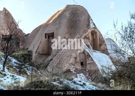 Snow-covered rock formations with cave dwellings stand near Uçhisar in Cappadocia, close to the Uçhisar Kalesi rock citadel. The Turkish name Uçhisar means "outer citadel" and refers to the prominent rock cone towering over the historic village centre; many of the old stone houses have since been converted into boutique hotels. Central Anatolia, Turkey. Stock Photo