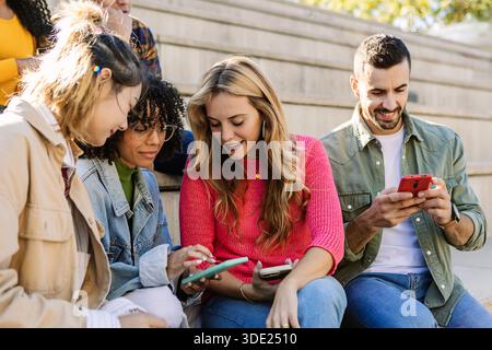 Group of diverse young student friends using smart phones outdoors Stock Photo