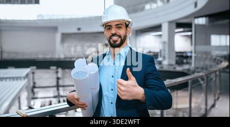 Construction Worker Stands With Blueprints in Building Site During Day Stock Photo