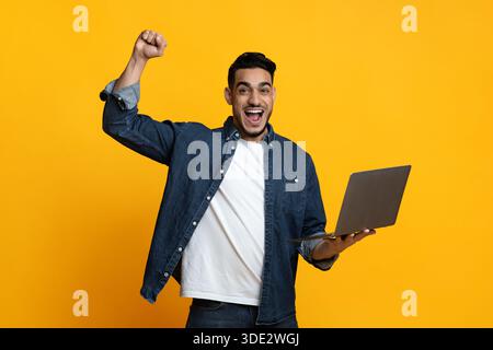 Emotional arab guy with new modern laptop on yellow Stock Photo