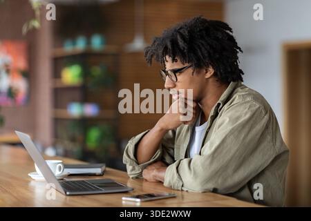 Young Black Male Entrepreneur Working With Laptop At Modern Coffeeshop Stock Photo