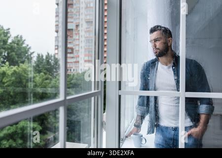 Depressed sad man looking through window, hoping for end of pandemic Stock Photo