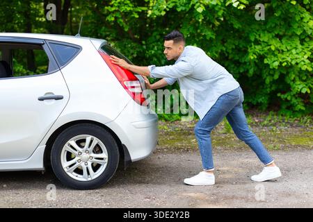 Arab guy pushing broken car, side view Stock Photo