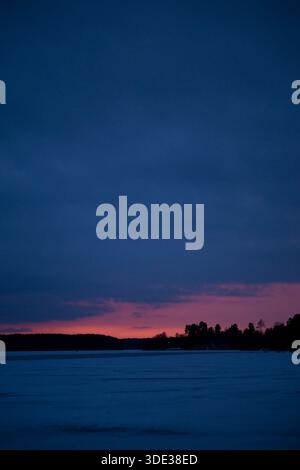 Beautiful purple warm sunset in a park near a frozen river, distant forest, blue clouds and snow Stock Photo