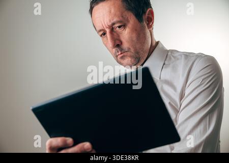 Concerned businessman analyzing financial data on a digital tablet, showing confusion and stress during business review, budgeting, or economic decisi Stock Photo