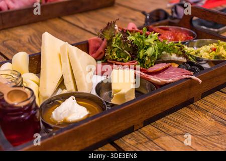 Traditional breakfast platter with cheese, cold cuts, greens, olives and spreads served on a wooden tray in a cafe or restaurant. Stock Photo