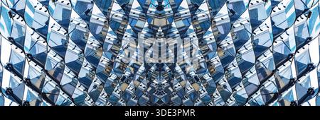 a modern architectural facade featuring a grid of irregular, diamond-shaped, reflective metallic panels. The panels create a dynamic, wave-like patter Stock Photo