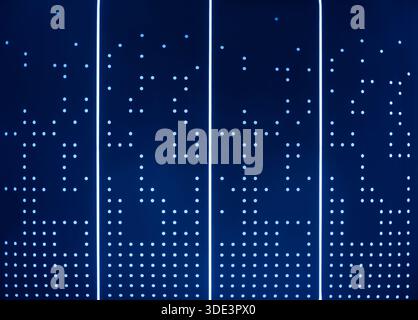 a modern, illuminated wall featuring vertical white LED light strips evenly spaced with small, bright LED dots. The background is a deep blue, creatin Stock Photo