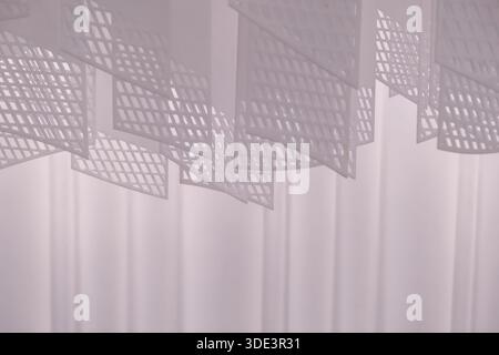 a series of geometric, lattice-patterned paper lanterns hanging from the ceiling. The lanterns are rectangular with a grid-like design, casting intric Stock Photo