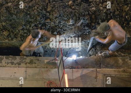Hard manual works when is need reconstruction under the street. Workers is working to repair the infrastructure behind light of lamp on night road. Sa Stock Photo
