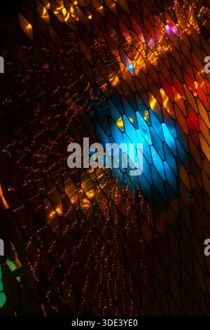 abstract, geometric wall made of hexagonal, glass-like tiles. The tiles reflect colorful lights creating a vibrant, shimmering effect. The overall tex Stock Photo