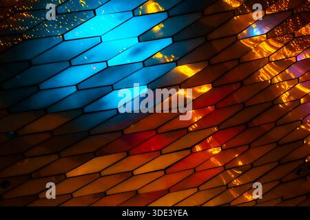 abstract, geometric wall made of hexagonal, glass-like tiles. The tiles reflect colorful lights creating a vibrant, shimmering effect. The overall tex Stock Photo