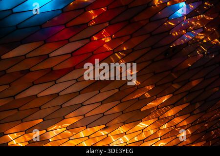 abstract, geometric wall made of hexagonal, glass-like tiles. The tiles reflect colorful lights creating a vibrant, shimmering effect. The overall tex Stock Photo