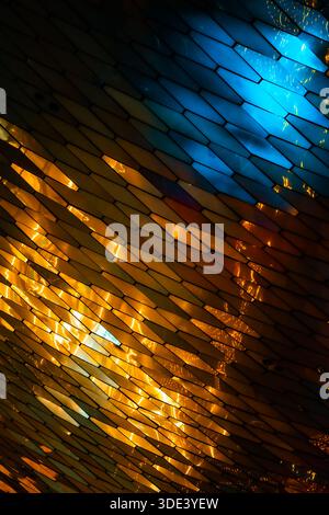 abstract, geometric wall made of hexagonal, glass-like tiles. The tiles reflect colorful lights creating a vibrant, shimmering effect. The overall tex Stock Photo