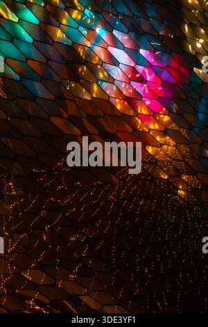 abstract, geometric wall made of hexagonal, glass-like tiles. The tiles reflect colorful lights creating a vibrant, shimmering effect. The overall tex Stock Photo