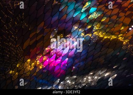abstract, geometric wall made of hexagonal, glass-like tiles. The tiles reflect colorful lights creating a vibrant, shimmering effect. The overall tex Stock Photo