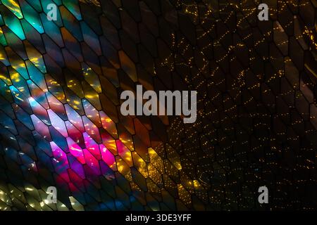 abstract, geometric wall made of hexagonal, glass-like tiles. The tiles reflect colorful lights creating a vibrant, shimmering effect. The overall tex Stock Photo