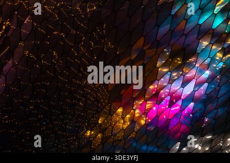 abstract, geometric wall made of hexagonal, glass-like tiles. The tiles reflect colorful lights creating a vibrant, shimmering effect. The overall tex Stock Photo