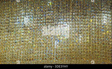 a shimmering, textured wall covered in numerous small, reflective, golden tinted glass beads. The beads are densely packed, creating a glittering, mos Stock Photo